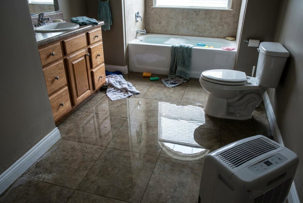 Flooded bathroom with standing water, toilet, bathtub, and dehumidifier during water damage cleanup